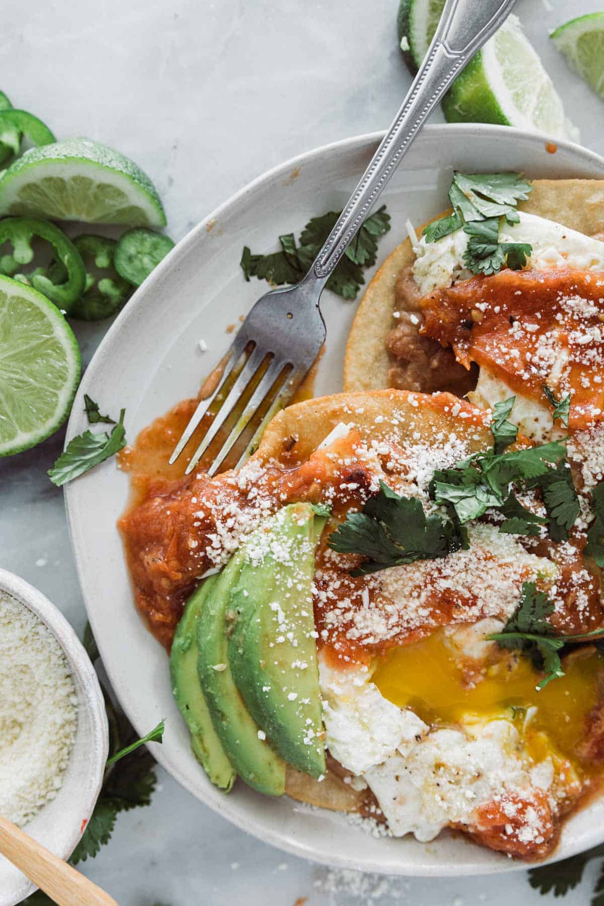 A plate of Mexican huevos rancheros with a fork resting on the side.