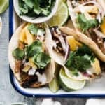 Tacos al pastor in a dish with lime wedges.