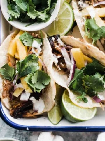 Tacos al pastor in a dish with lime wedges.