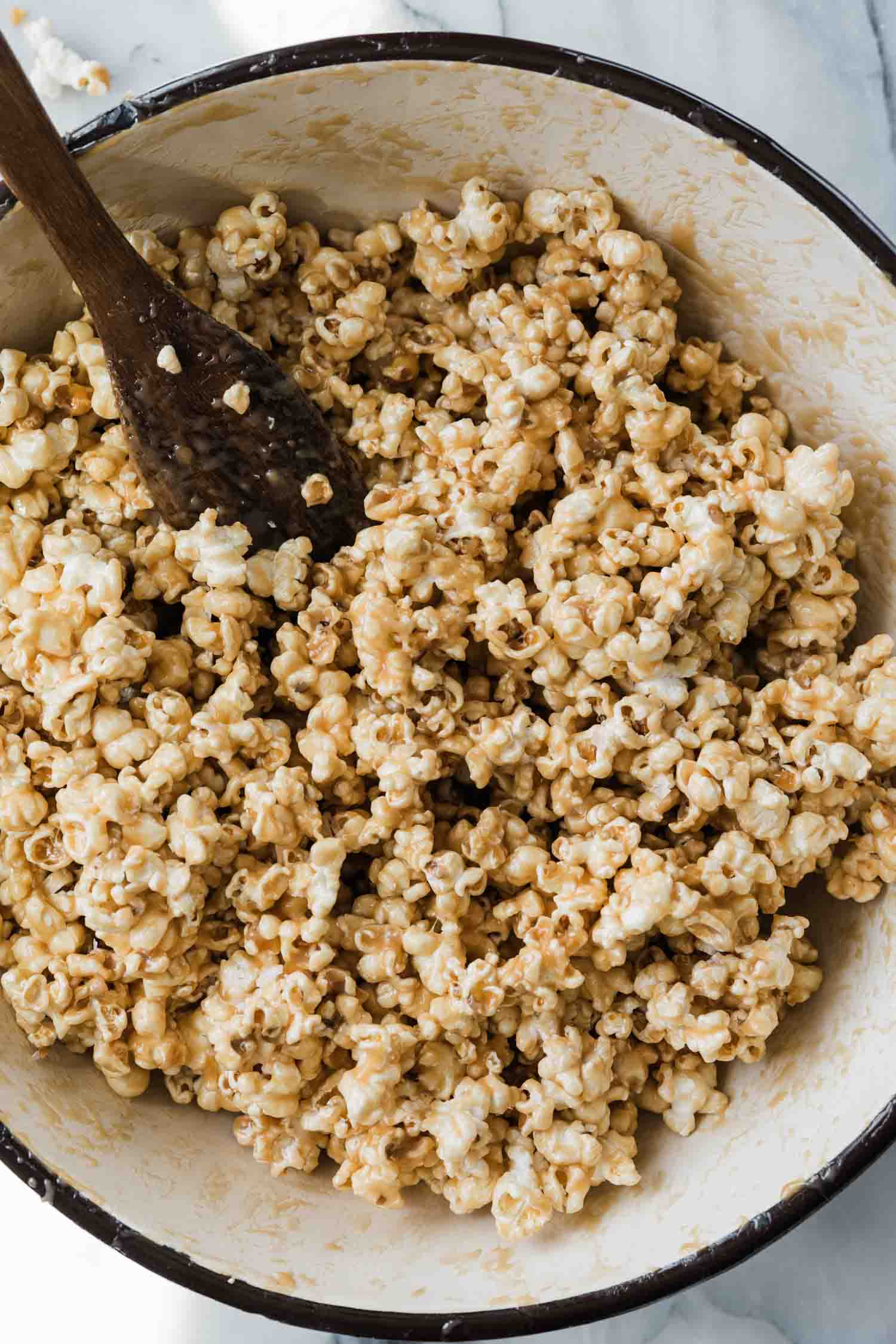Caramel popcorn in a Dutch oven with a wooden spoon in the pot. 