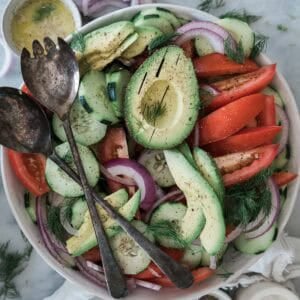 Cucumber tomato onion salad with a fork and spoon on top of the bowl.