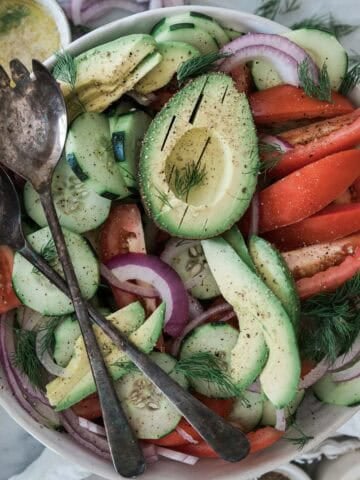Cucumber tomato onion salad with a fork and spoon on top of the bowl.