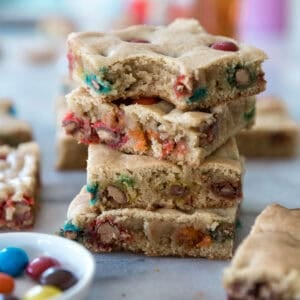 A stack of M&M blondies recipe on a counter with a bowl of candy to the side.