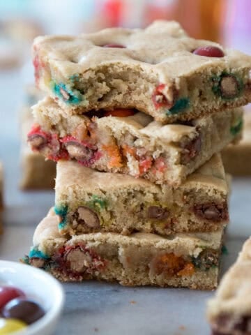 A stack of M&M blondies recipe on a counter with a bowl of candy to the side.