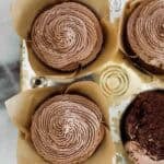 Chocolate cupcakes in a muffin tin in parchment paper liners.
