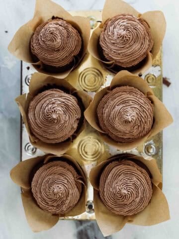 Six cupcakes in a pan with a chocolate icing piped on them.