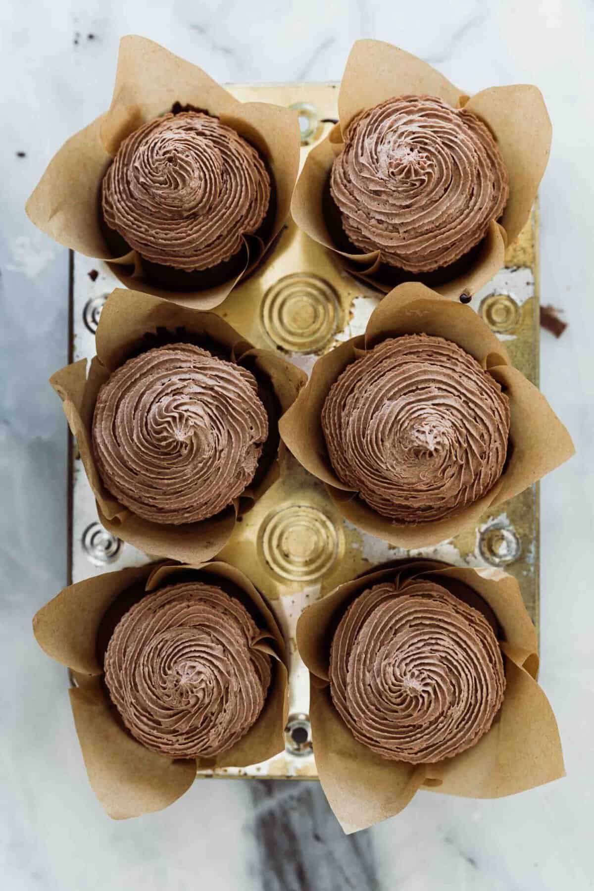 Six cupcakes in a pan with a chocolate icing piped on them. 