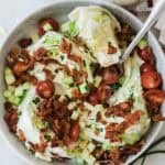 A bowl of wedge salad on a table topped with bacon and a fork resting in the bowl.