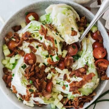 A bowl of wedge salad on a table topped with bacon and a fork resting in the bowl.