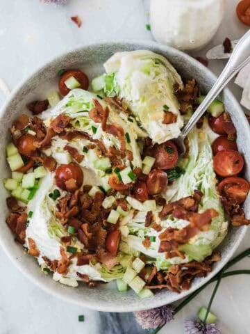 A bowl of wedge salad on a table topped with bacon and a fork resting in the bowl.