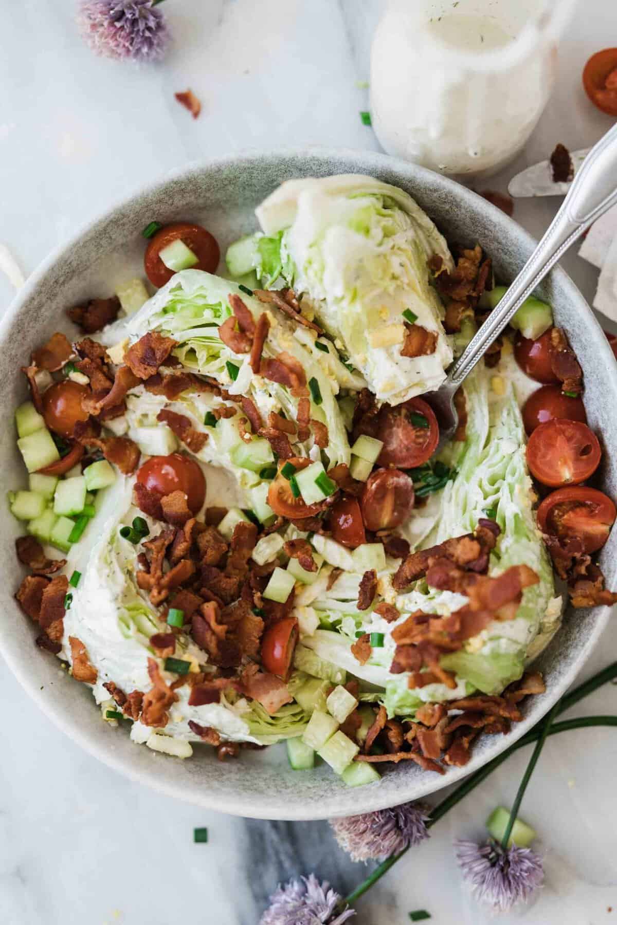 A fork mixing the salad with tomatoes, bacon and cucumbers.