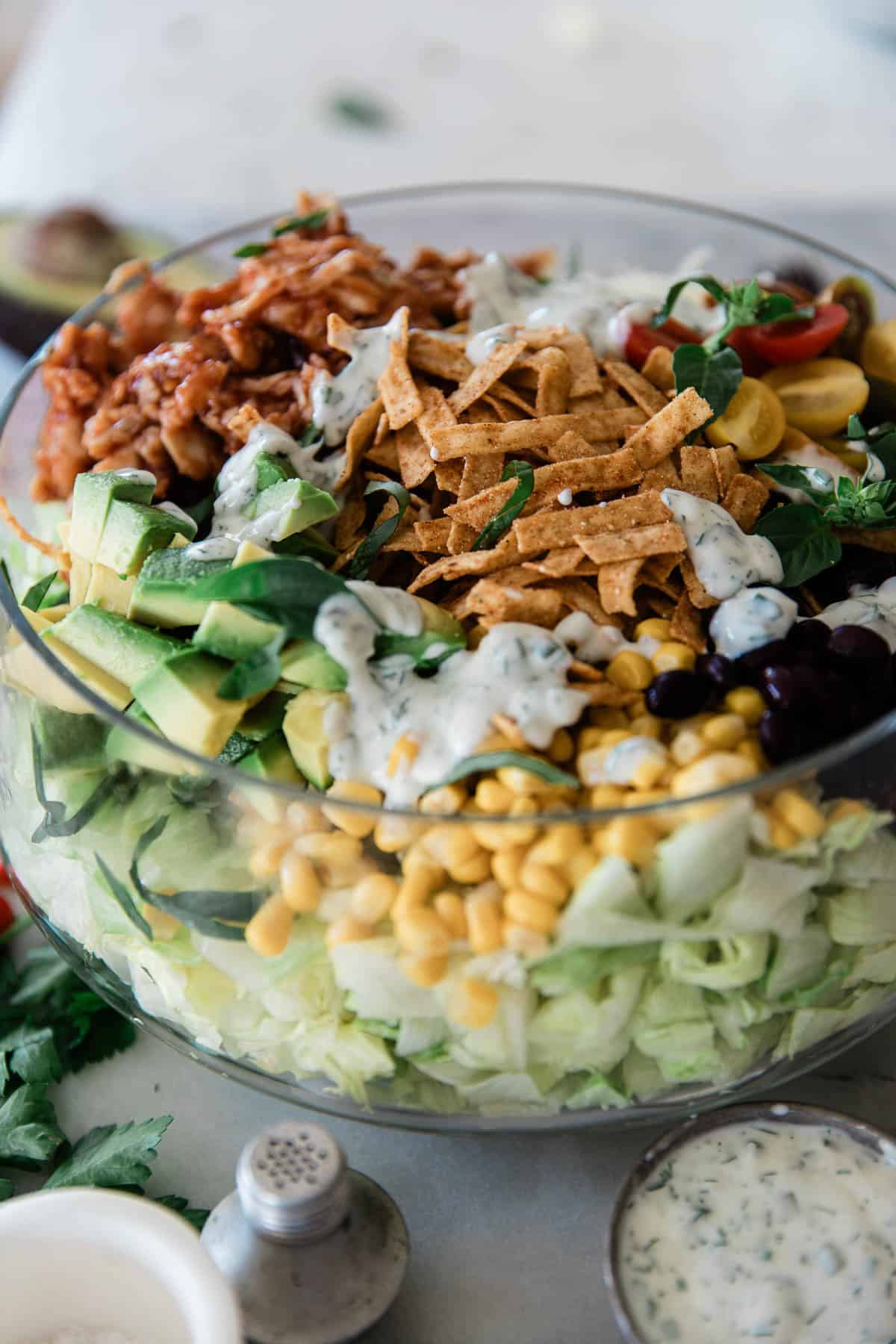 A clear bowl with salad with BBQ chicken.