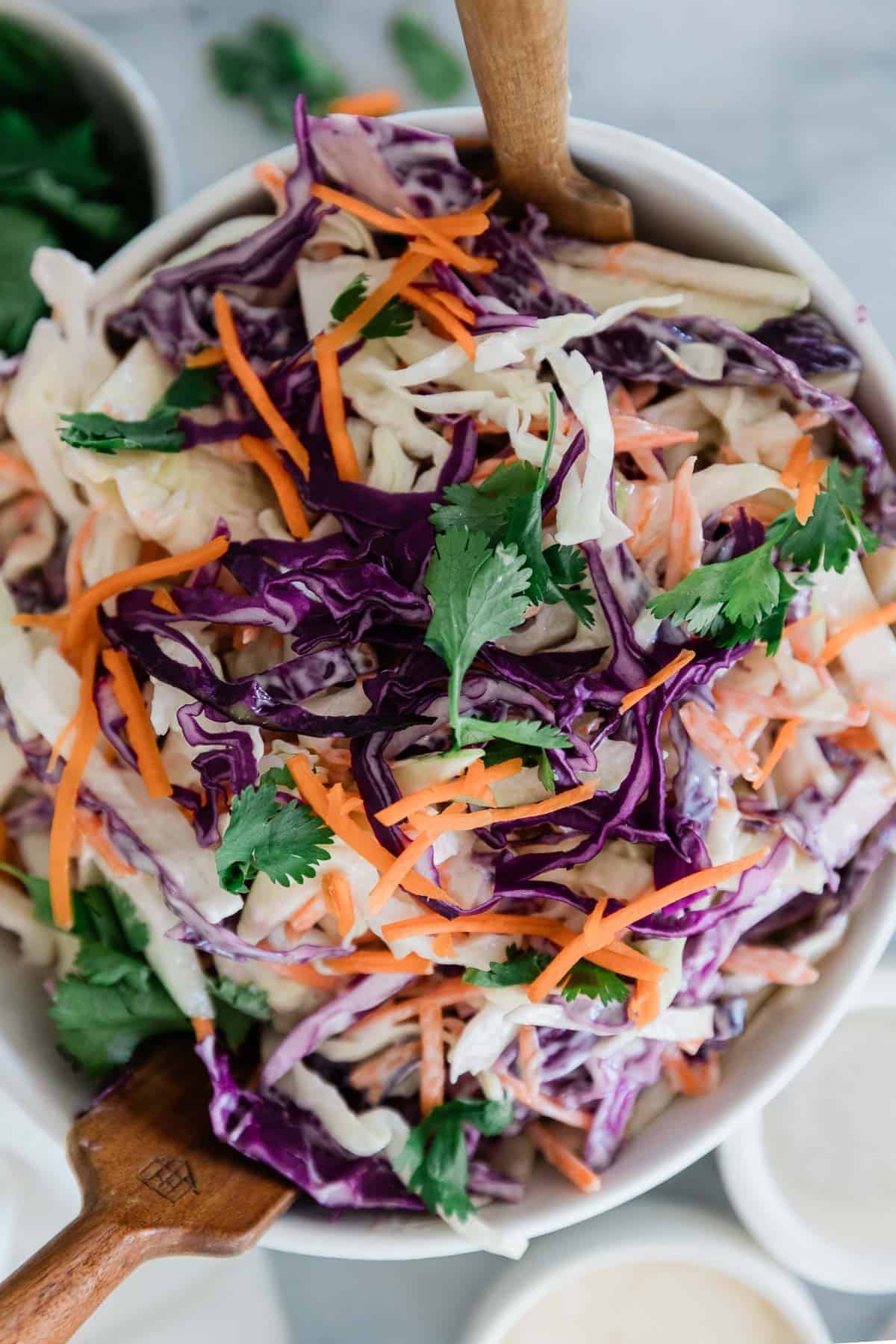 Coleslaw with apples being mixed with wooden spoons.