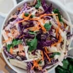 Coleslaw with apple, carrots, cabbage, and parsley garnished on top.