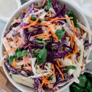 Coleslaw with apple, carrots, cabbage, and parsley garnished on top.