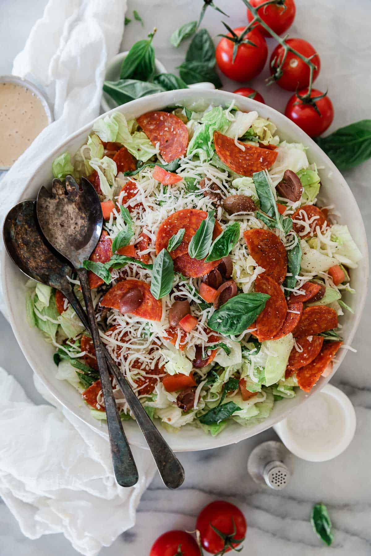 A bowl filled with chopped Italian salad with pepperoni and two spoons on the side.