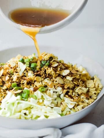 Pouring dressing over a bowl of ramen cabbage salad.
